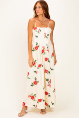 woman wearing a cream floral maxi dress with red roses and thin straps, standing against a white background