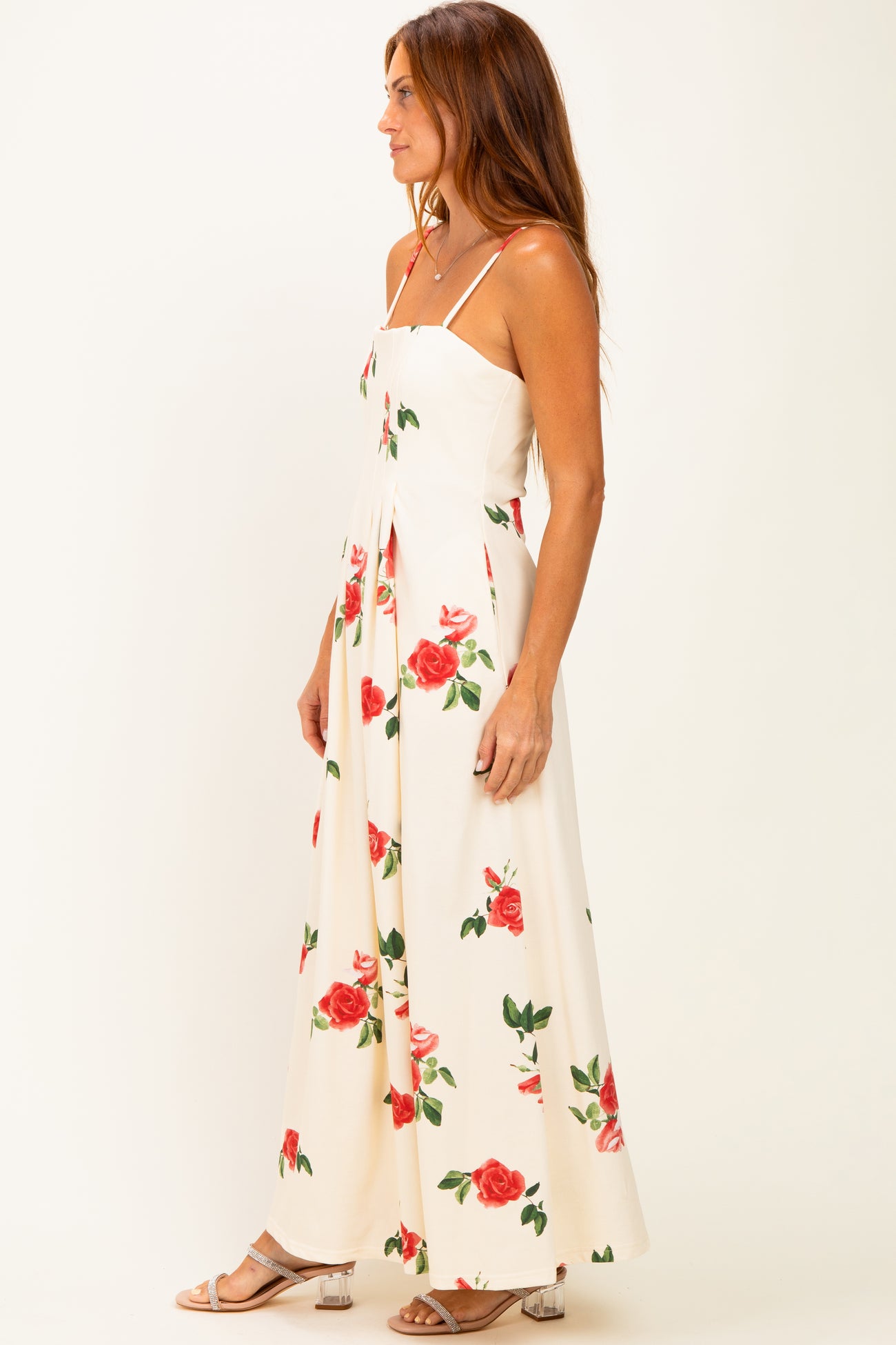 woman wearing a floral maxi dress with red roses on a cream background and spaghetti straps