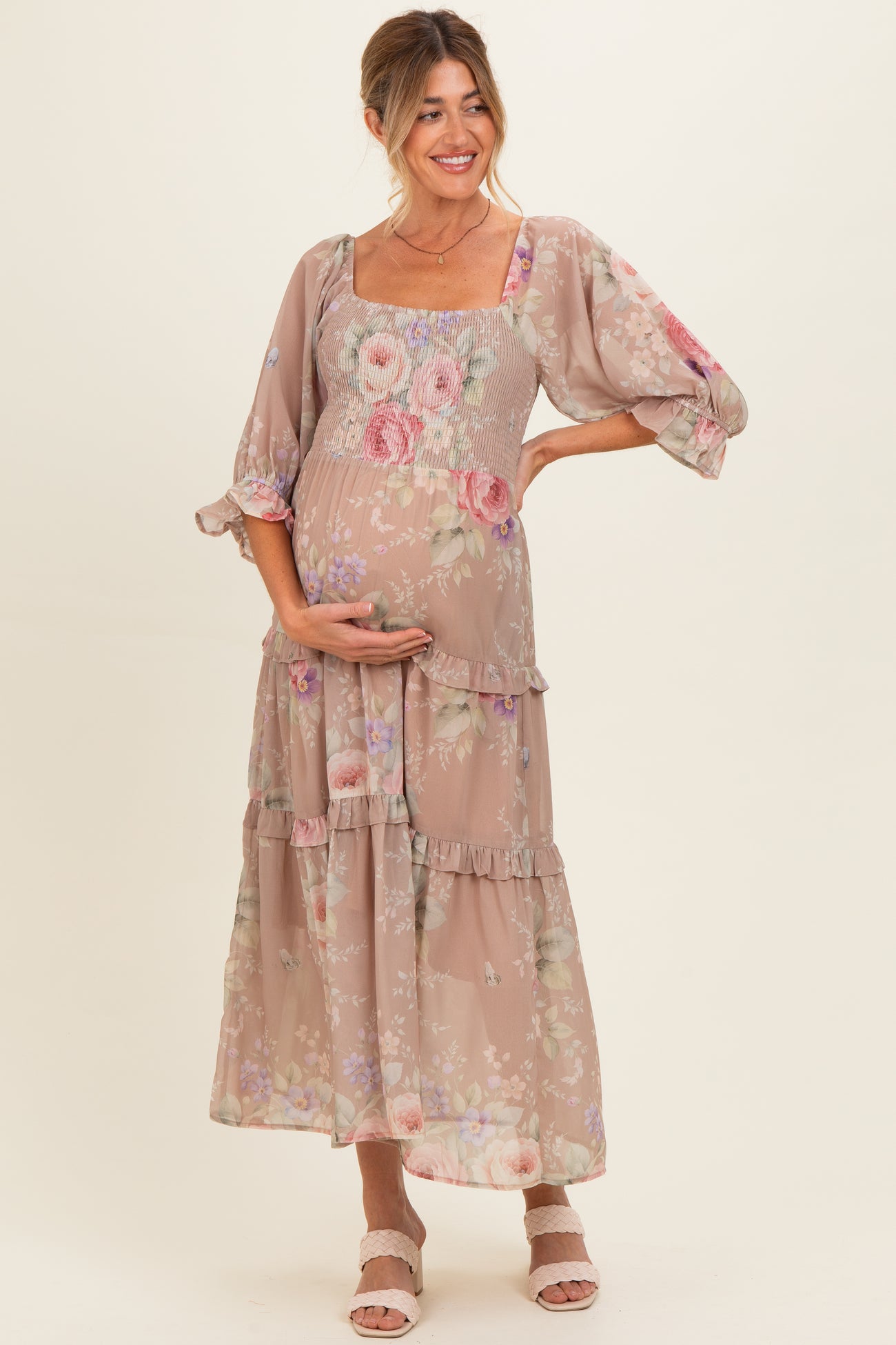 woman wearing a floral print maternity maxi dress with puff sleeves and a fitted bodice, holding her baby bump