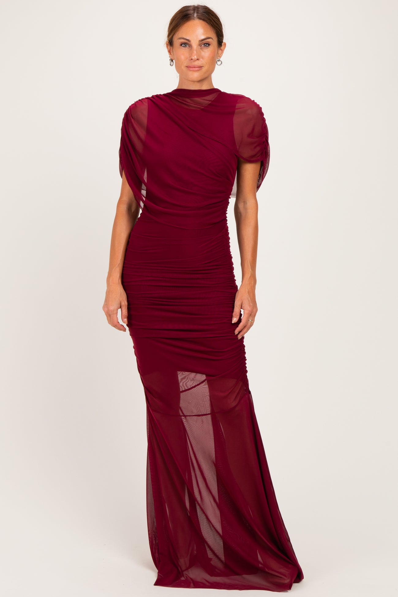 woman wearing a burgundy ruched evening gown with sheer sleeves and a fitted silhouette