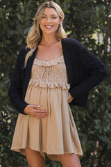 woman wearing a navy cardigan over a beige ruffled maternity dress and holding her baby bump
