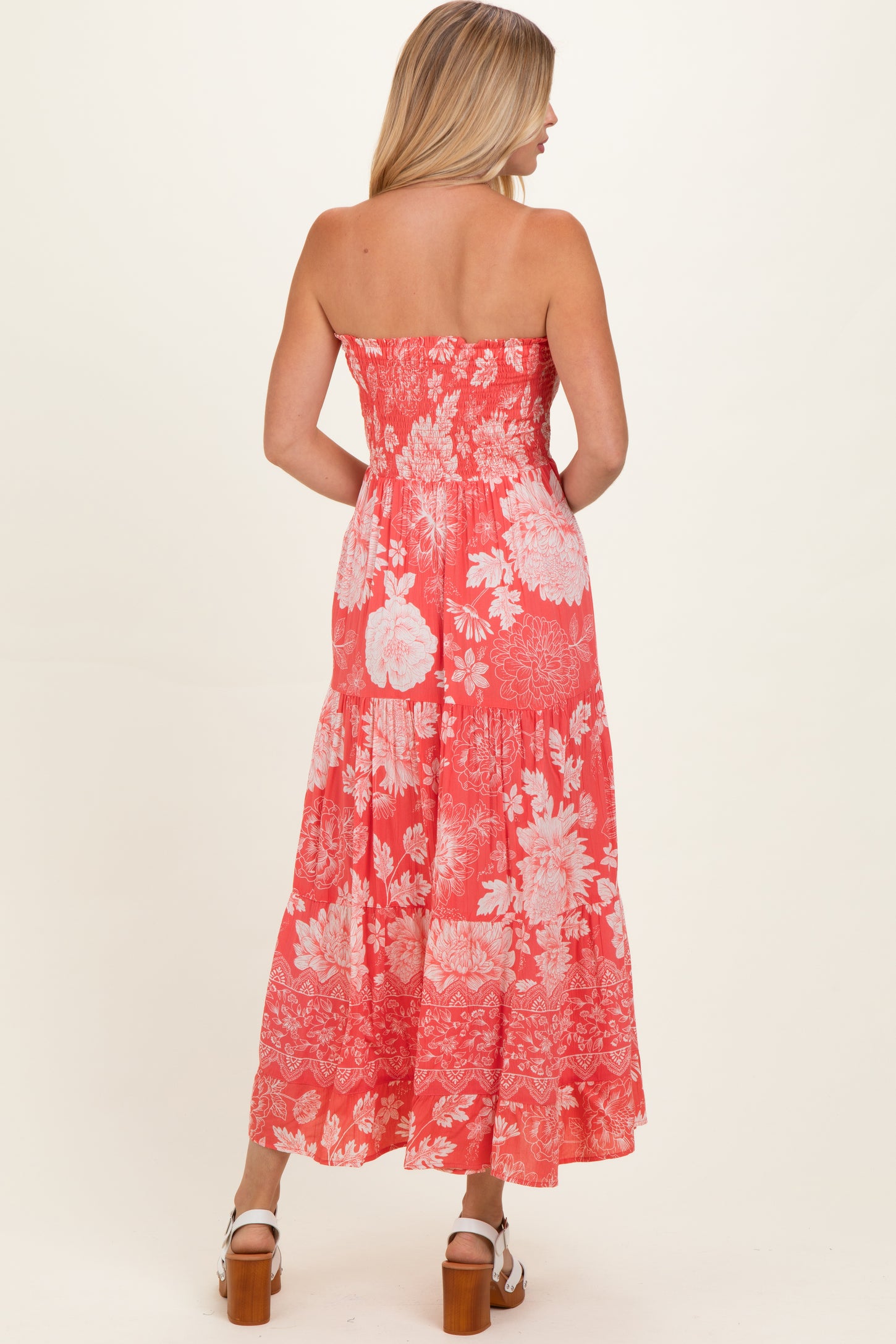 woman wearing a coral strapless maxi dress with floral print, showing a tiered skirt and back view
