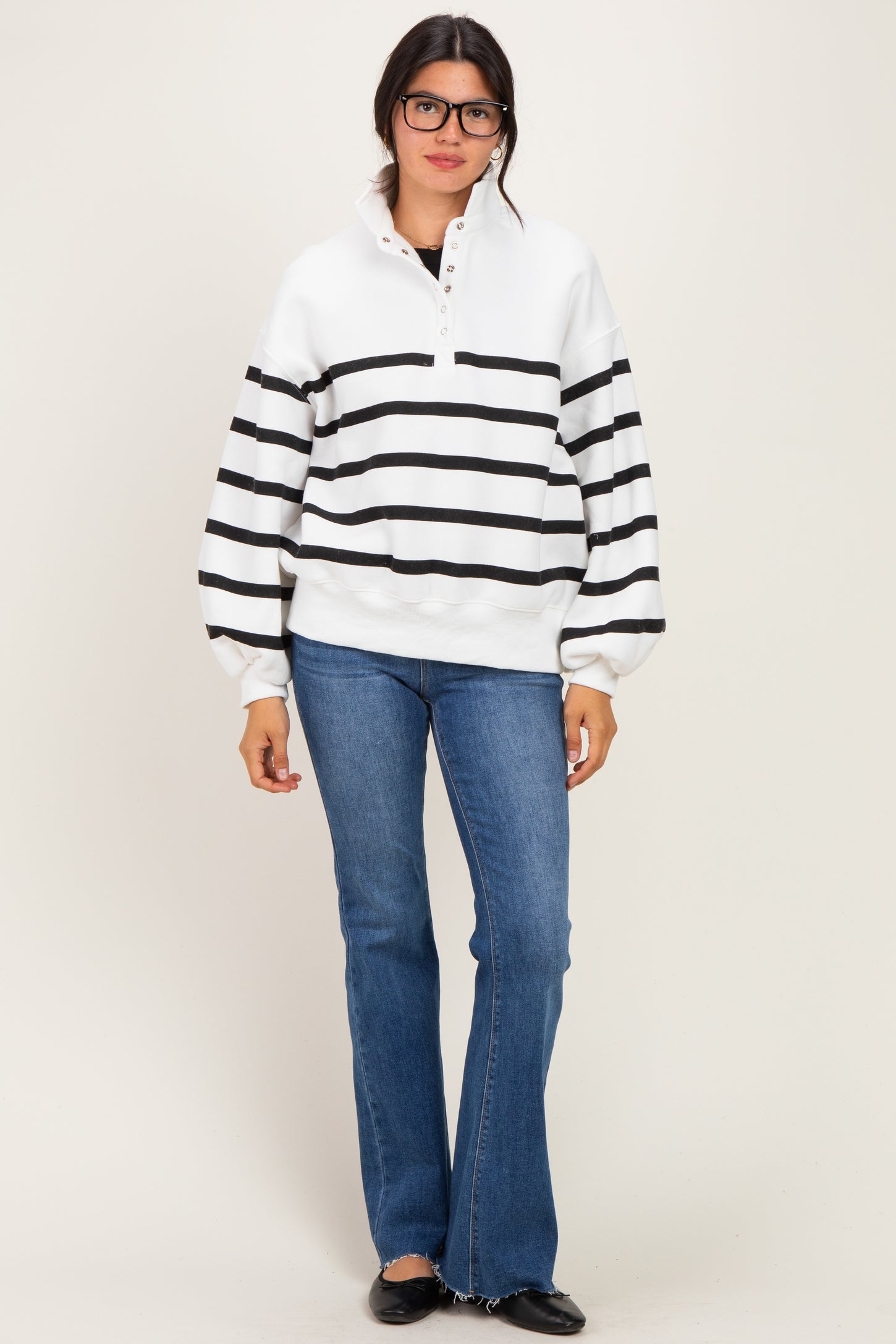 woman wearing a white and black striped pullover with a collar, paired with flared jeans and black flats