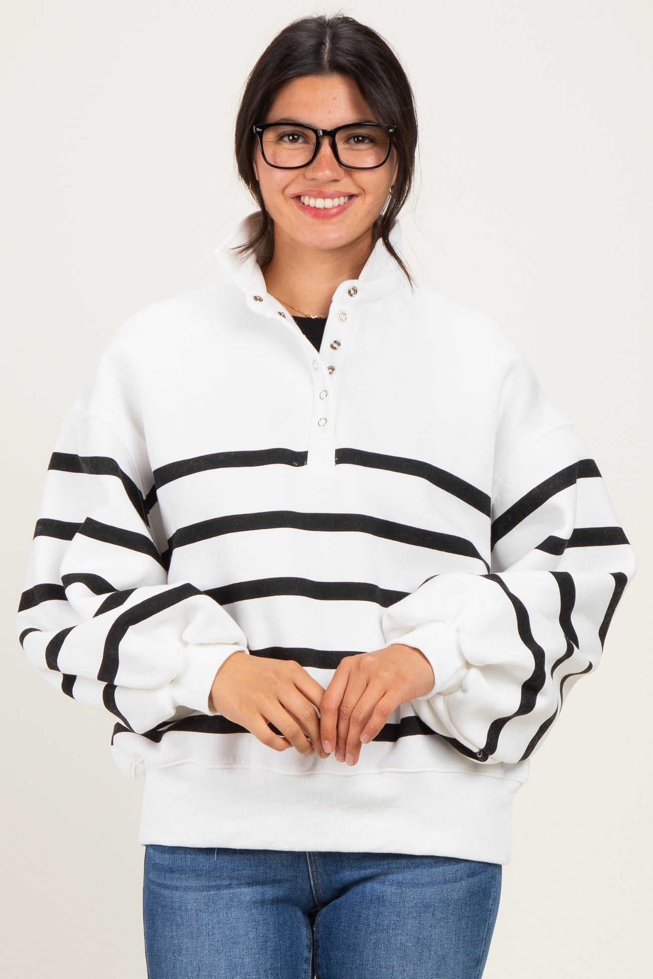 woman wearing a white and black striped pullover sweatshirt with a high collar and button detailing, smiling and wearing glasses