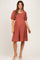 woman wearing a rust-colored maternity dress with black polka dots and puff sleeves