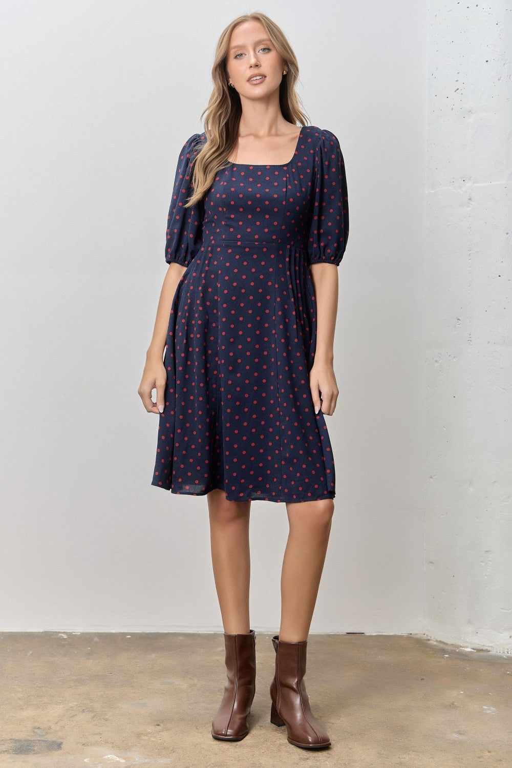 woman wearing a navy blue short sleeve dress with red polka dots and puff sleeves, paired with brown ankle boots