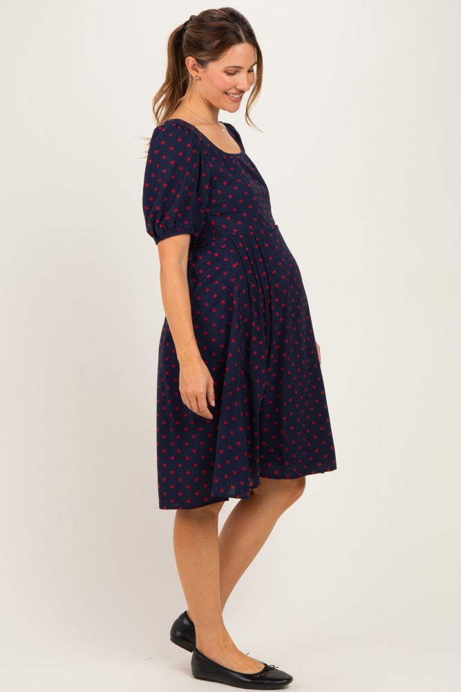 woman wearing a navy blue maternity dress with red polka dots and a fitted bodice, showcasing her baby bump