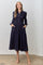 woman wearing a navy blue midi dress with puff sleeves, smocked bodice, and red polka dots, featuring pockets
