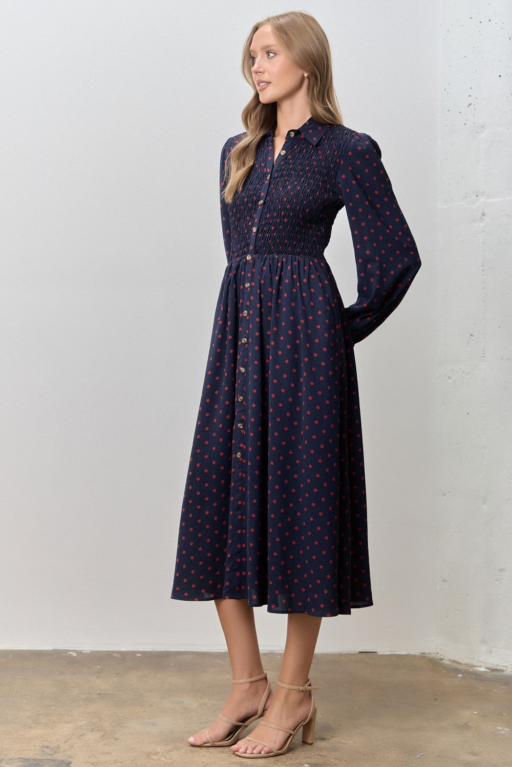 woman wearing a navy blue long sleeve midi dress with red polka dots and a smocked bodice
