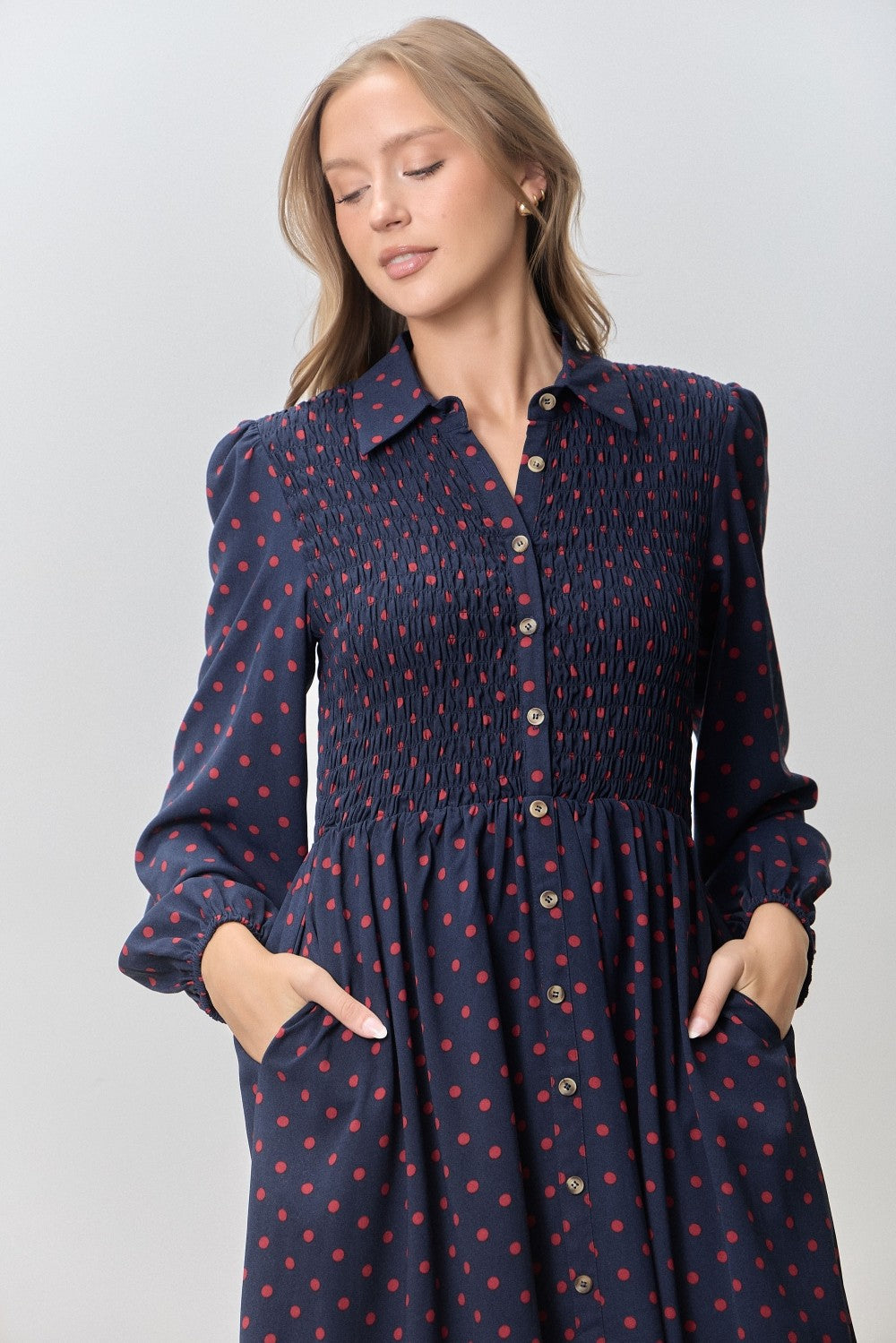 woman wearing a navy polka dot dress with a smocked bodice, button-front, and side pockets