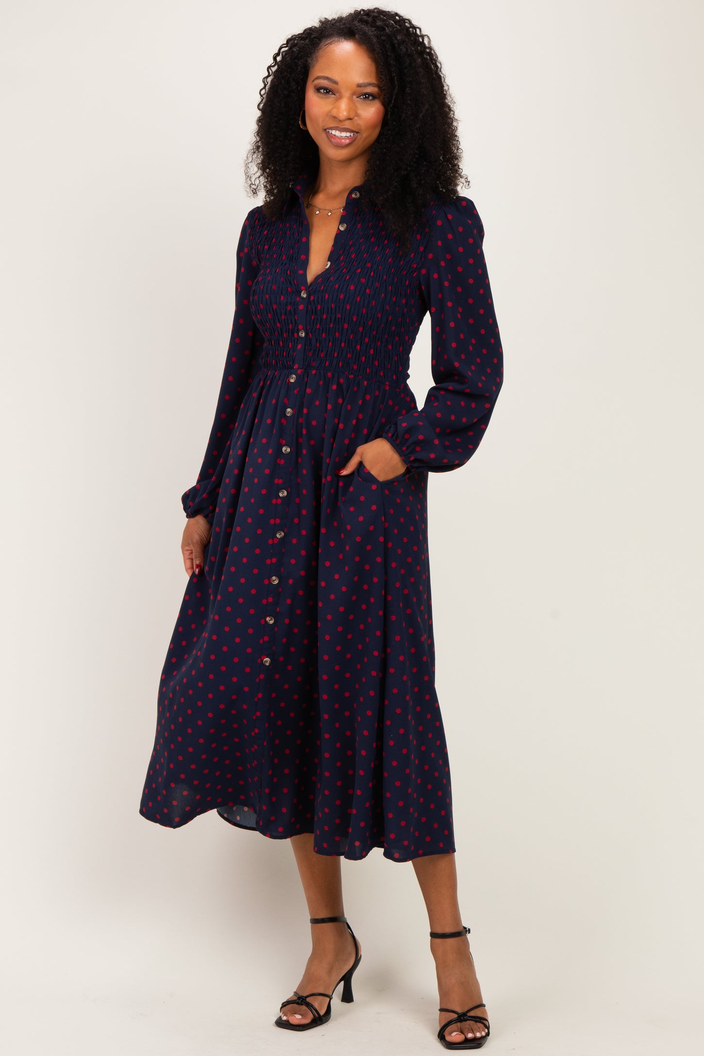 woman wearing a navy midi dress with red polka dots and long puff sleeves, featuring a smocked bodice and pockets
