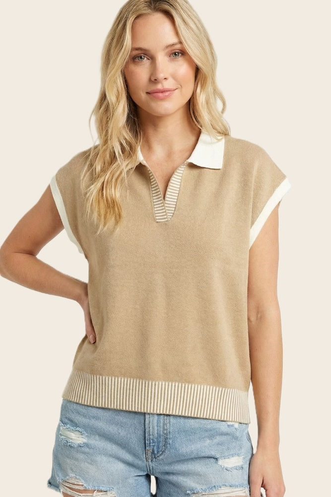 woman wearing a beige short sleeve sweater with a white collar and striped hem, paired with denim shorts