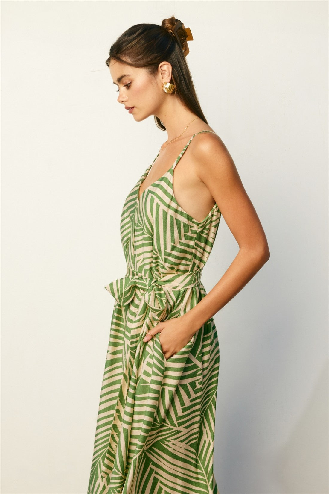 woman wearing a green tropical print spaghetti strap dress with a tied waist and side pockets