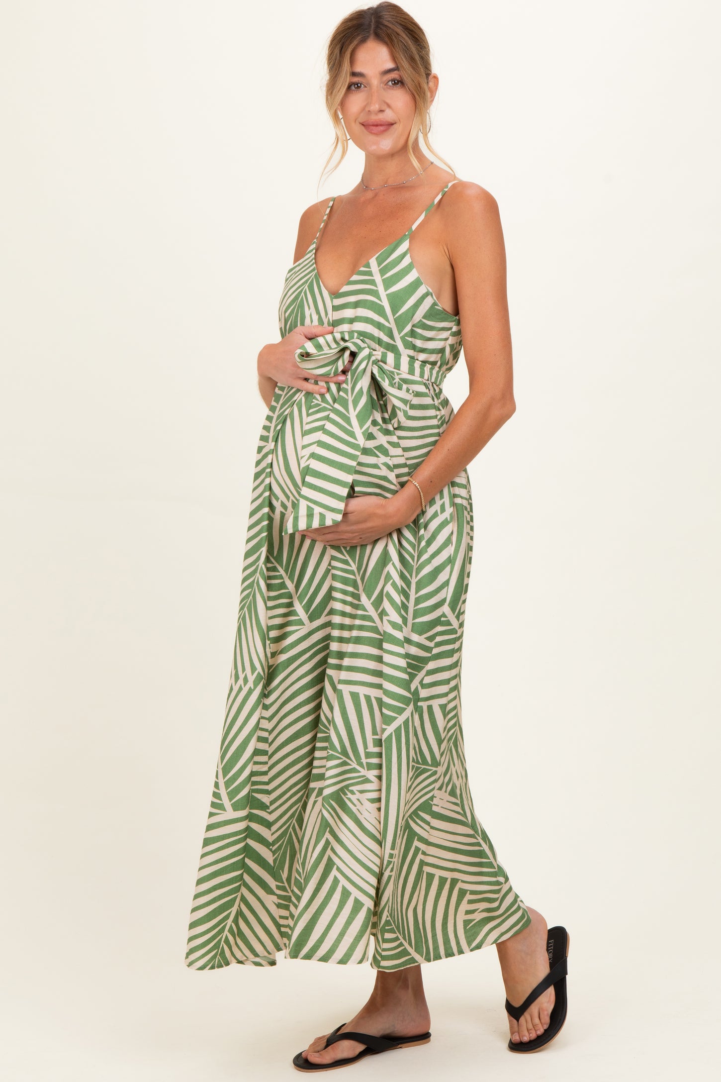woman wearing a green and white palm leaf print maternity maxi dress and holding her baby bump