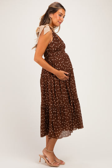 woman wearing a brown polka dot maternity dress with tie shoulder details and holding her baby bump