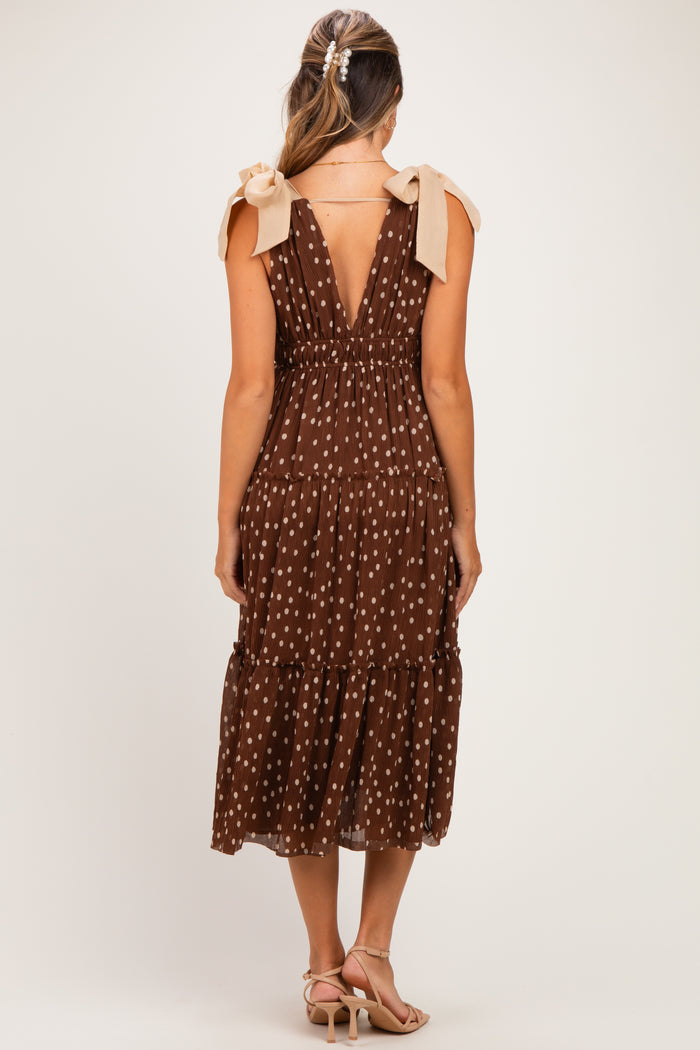 woman wearing a brown polka dot maternity dress with tie shoulder straps and a tiered skirt, revealing a baby bump from behind