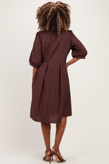 woman wearing a burgundy maternity dress with puff sleeves and a pleated back design