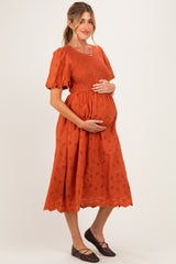 woman wearing an orange maternity dress with puff sleeves and a smocked bodice, holding her baby bump
