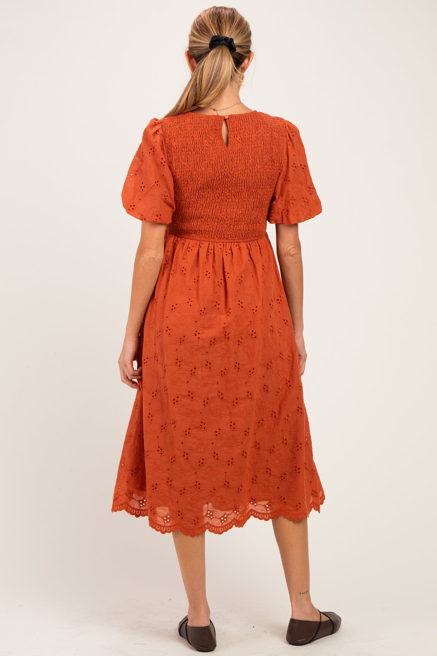 woman wearing an orange maternity dress with short puff sleeves and embroidery details, showing the back view
