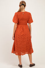 woman wearing an orange maternity dress with short puff sleeves and embroidery details, showing the back view