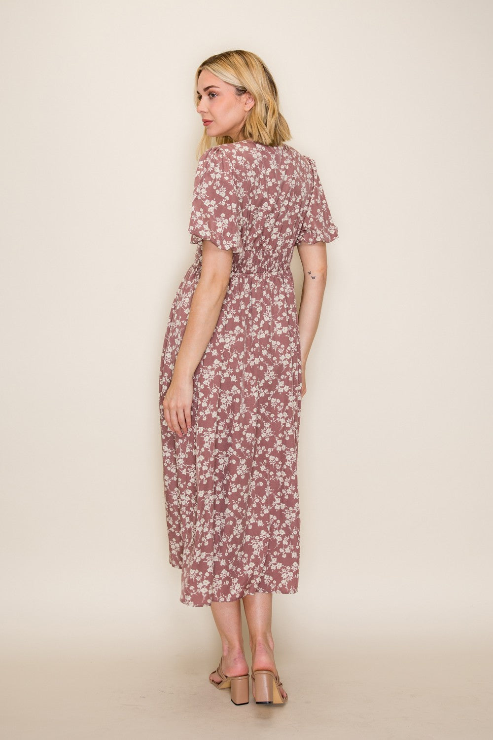 woman wearing a pink floral maxi dress with short sleeves, standing with her back to the camera