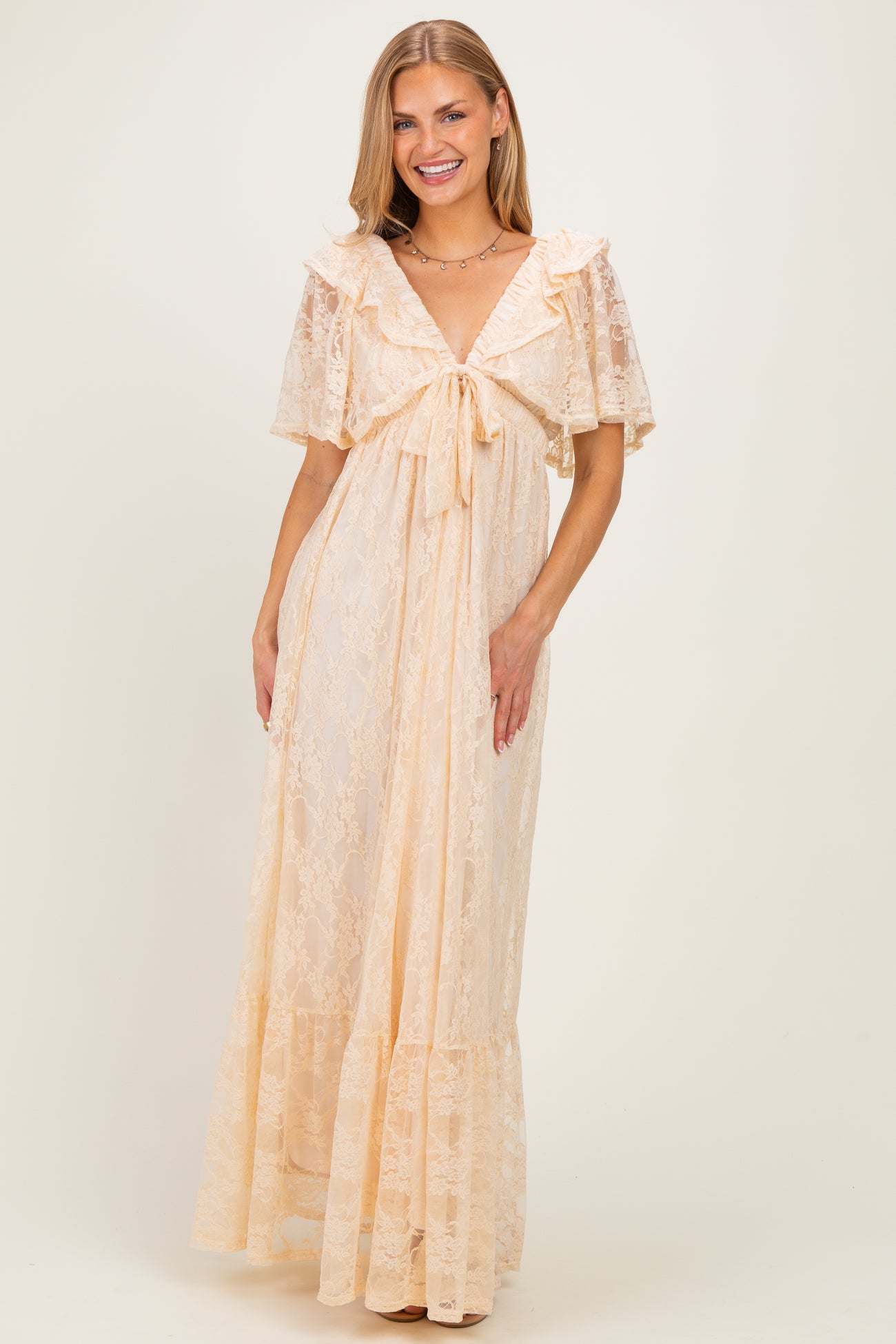 woman wearing a light peach lace maxi dress with a tie front and ruffled sleeves