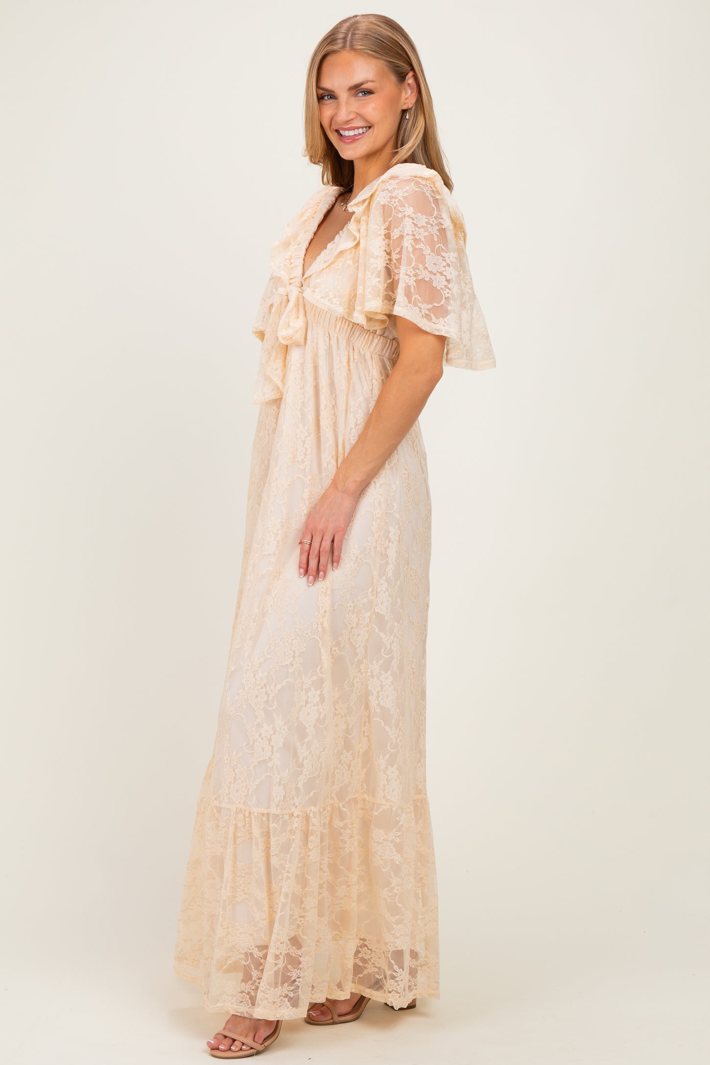 woman wearing a beige lace maxi dress with ruffle details and short flutter sleeves