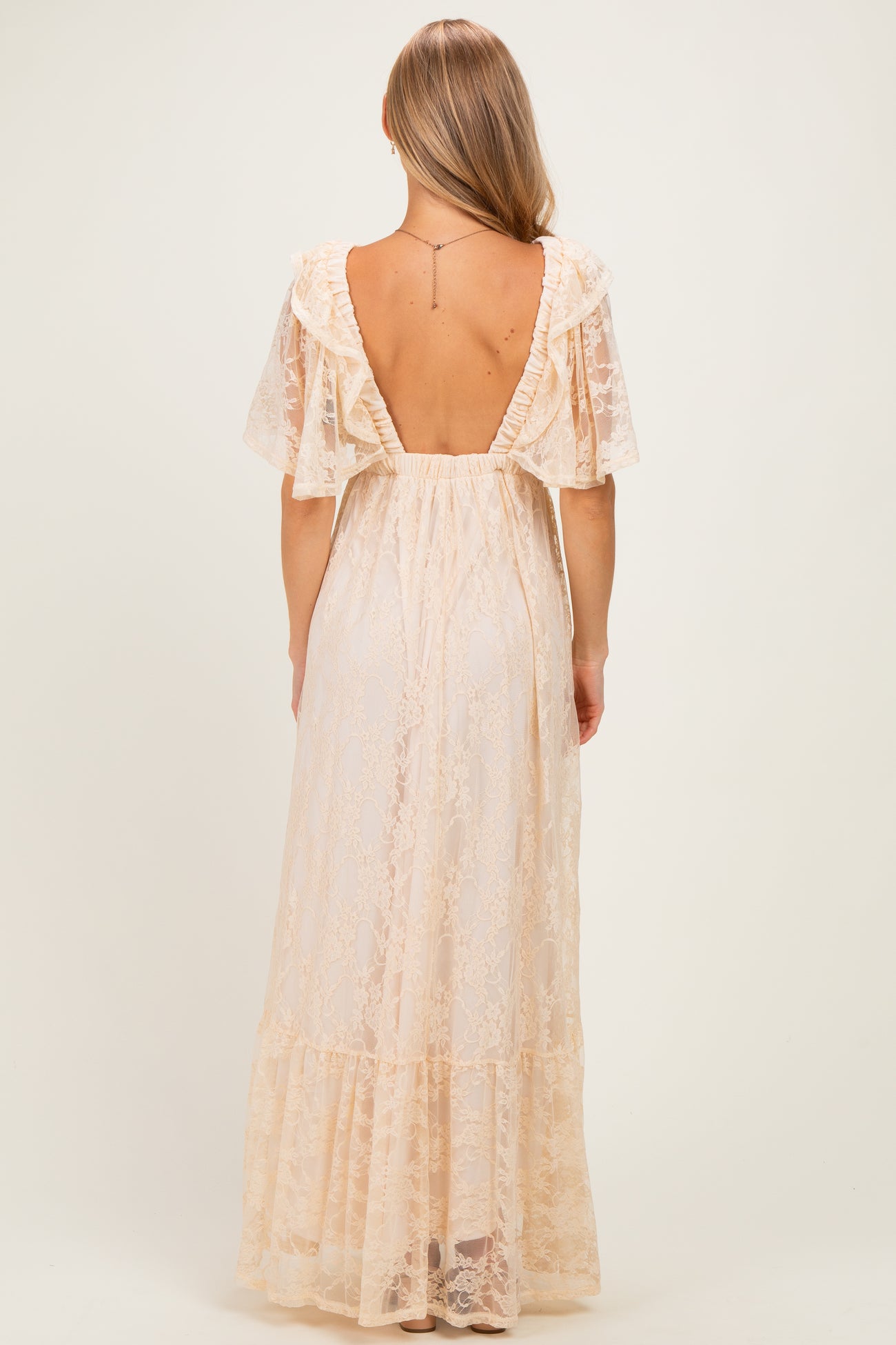 woman wearing a backless sheer lace maxi dress with flutter sleeves and a tiered hem