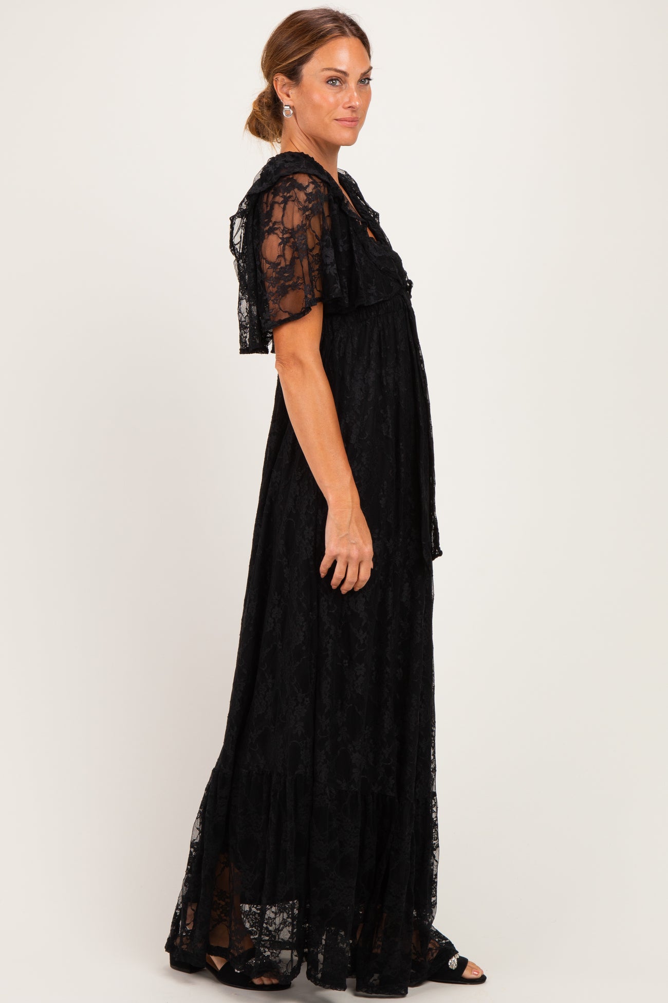 woman wearing a black lace maxi dress with short flutter sleeves and tiered skirt details