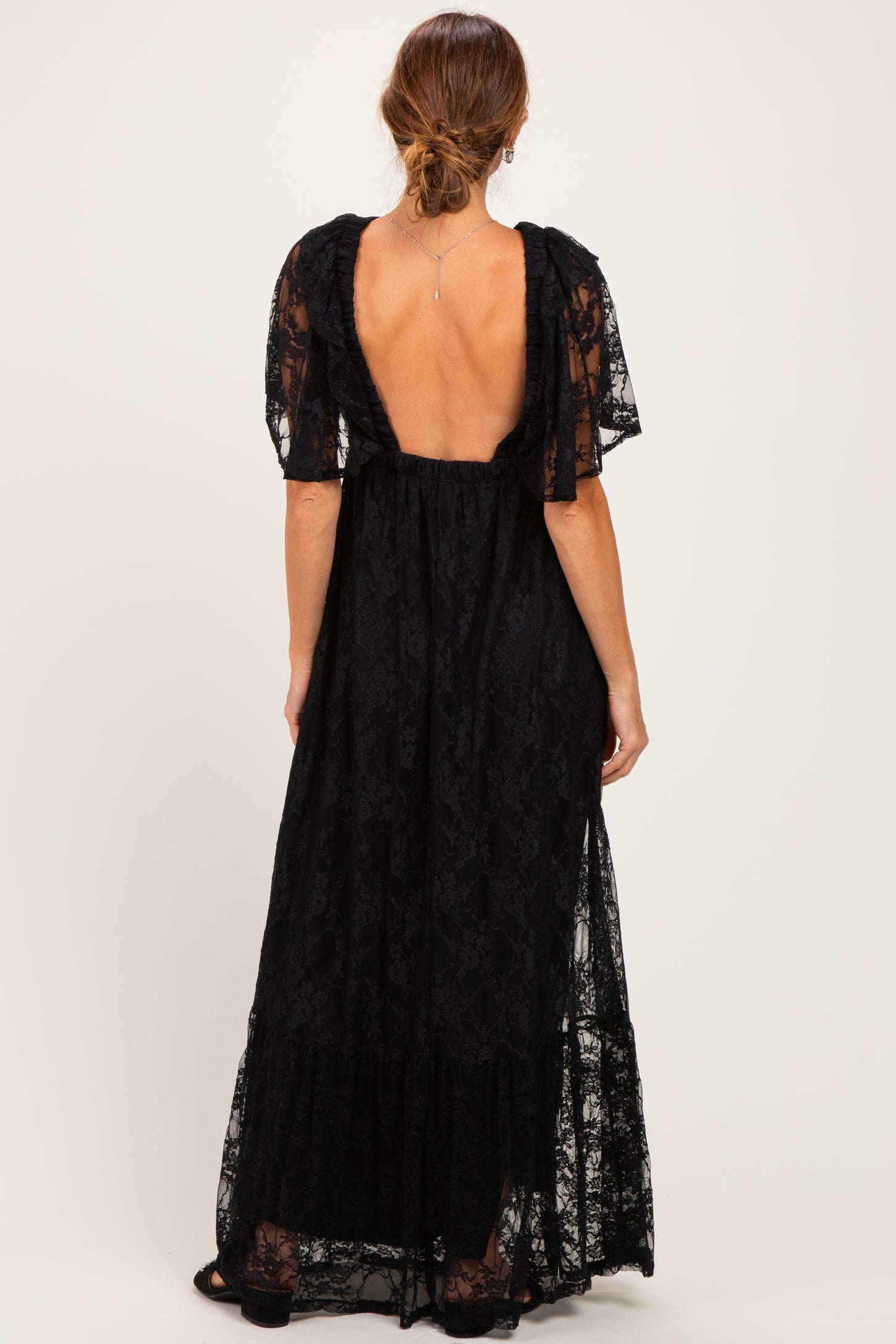 woman wearing a black lace maxi dress with short flutter sleeves and a deep back cutout