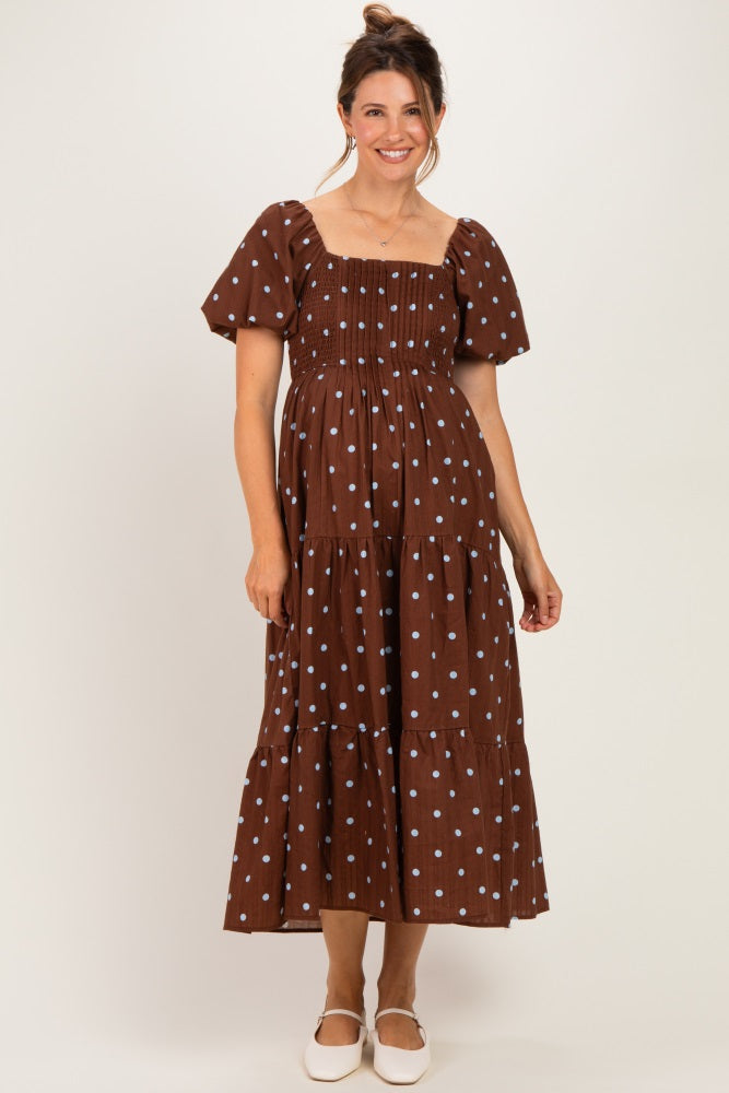 woman wearing a brown maternity dress with white polka dots and puff sleeves, standing and smiling