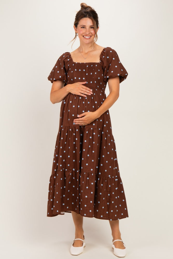 woman wearing a brown polka dot maternity dress with puff sleeves and a tiered skirt, holding her baby bump