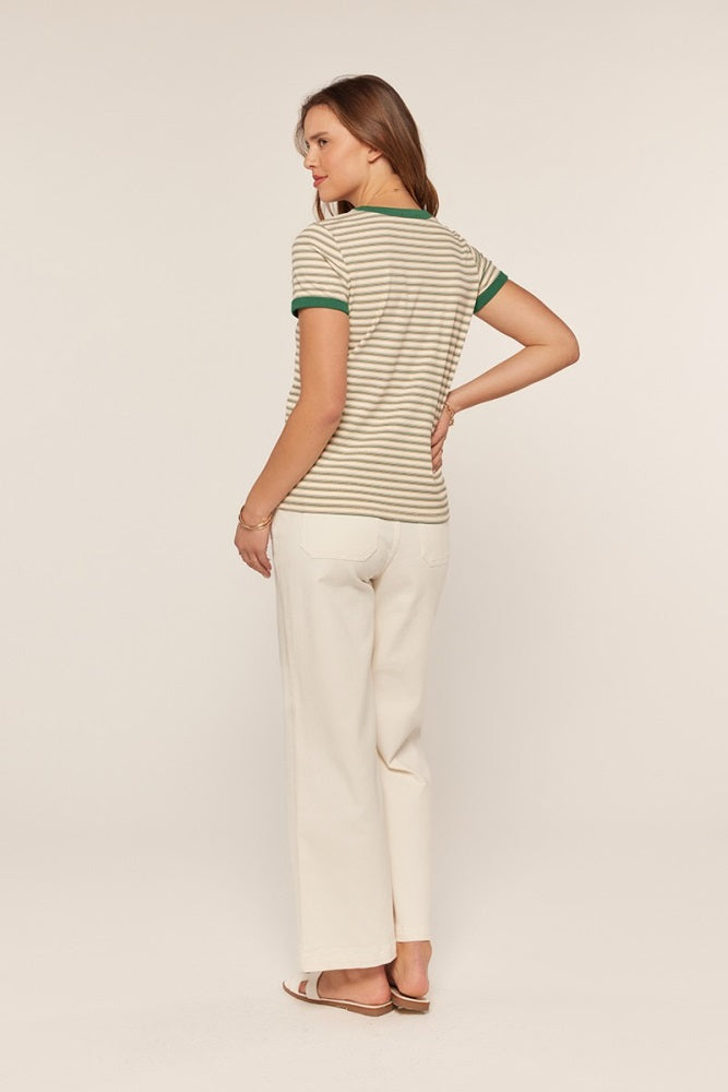 woman wearing a beige and white striped t-shirt with green trim and off-white wide-leg pants, standing with her back to the camera