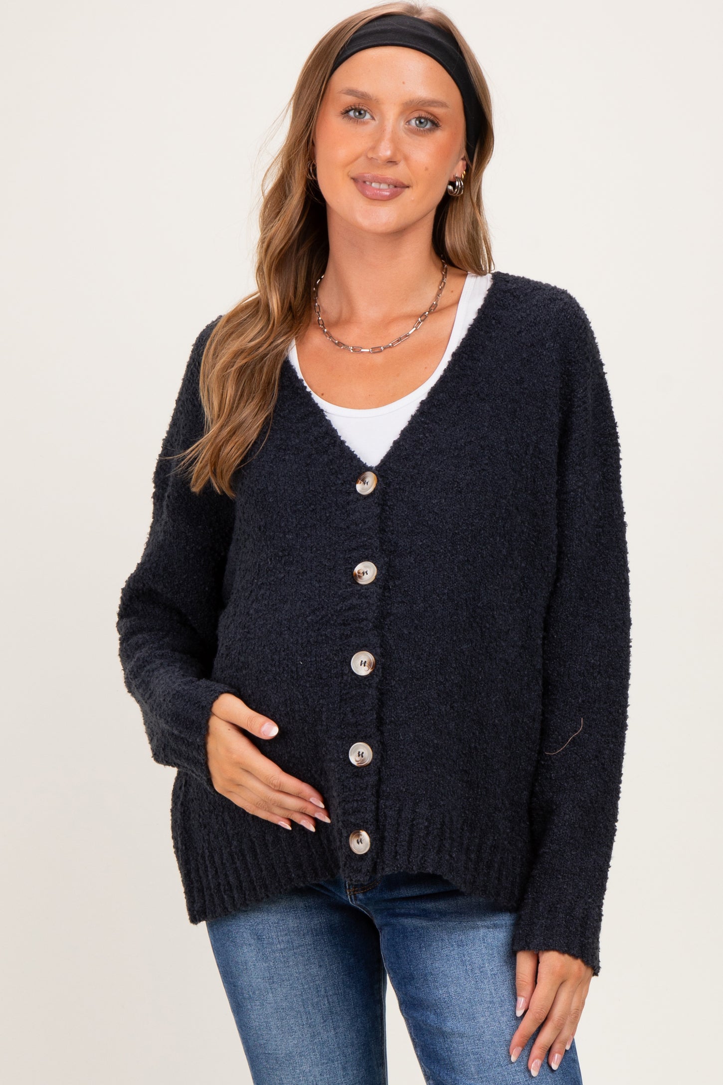 woman wearing a dark navy maternity cardigan with buttons, holding her baby bump, paired with a white top and jeans