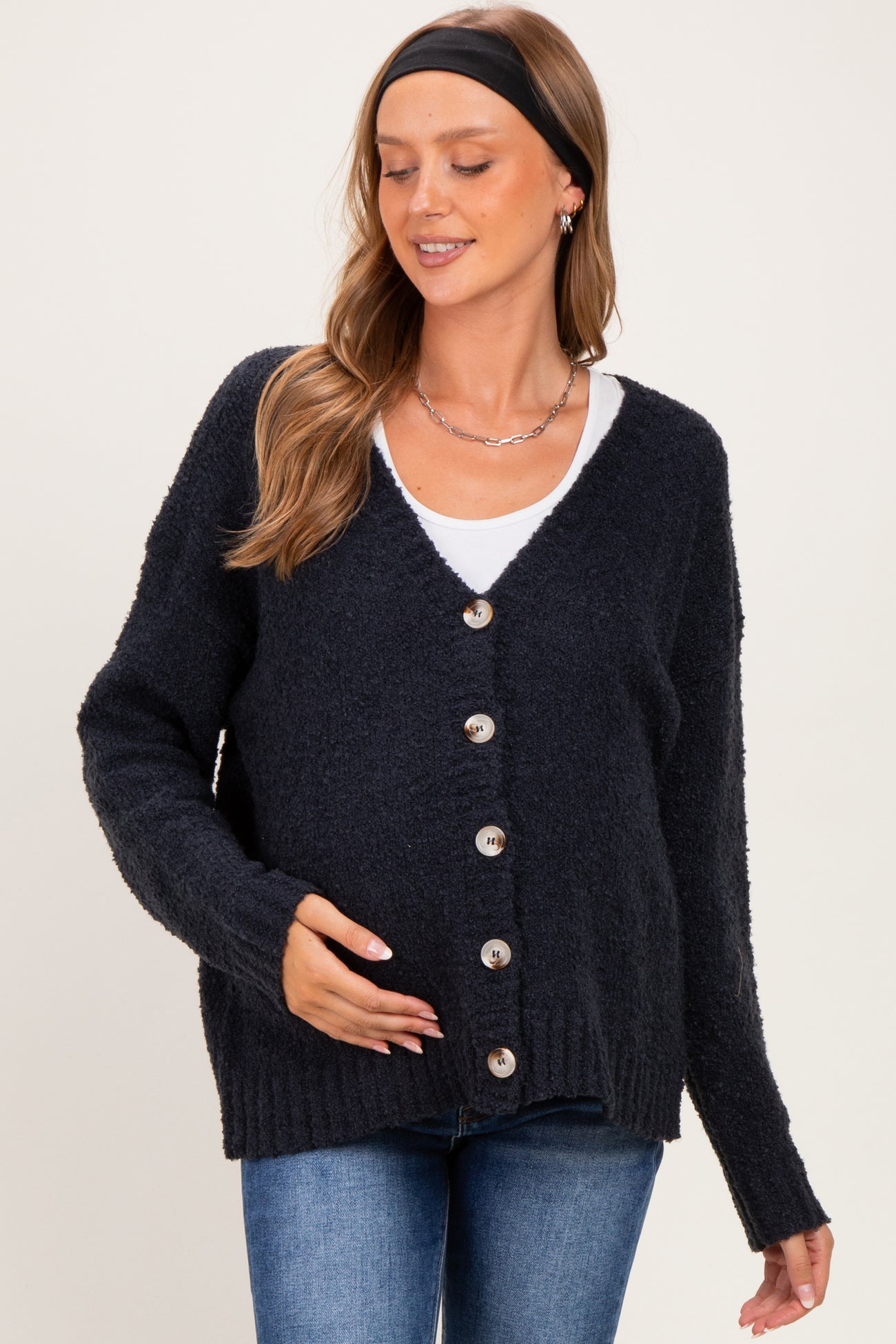 woman wearing a navy blue maternity cardigan with buttons, holding her baby bump and paired with a white top and jeans