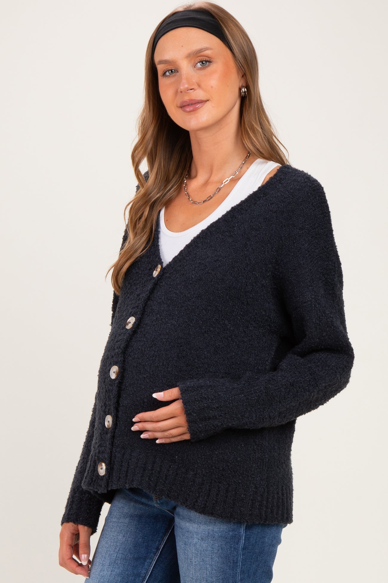 woman wearing a dark navy maternity cardigan with buttons, gently holding her baby bump, paired with a white top and jeans