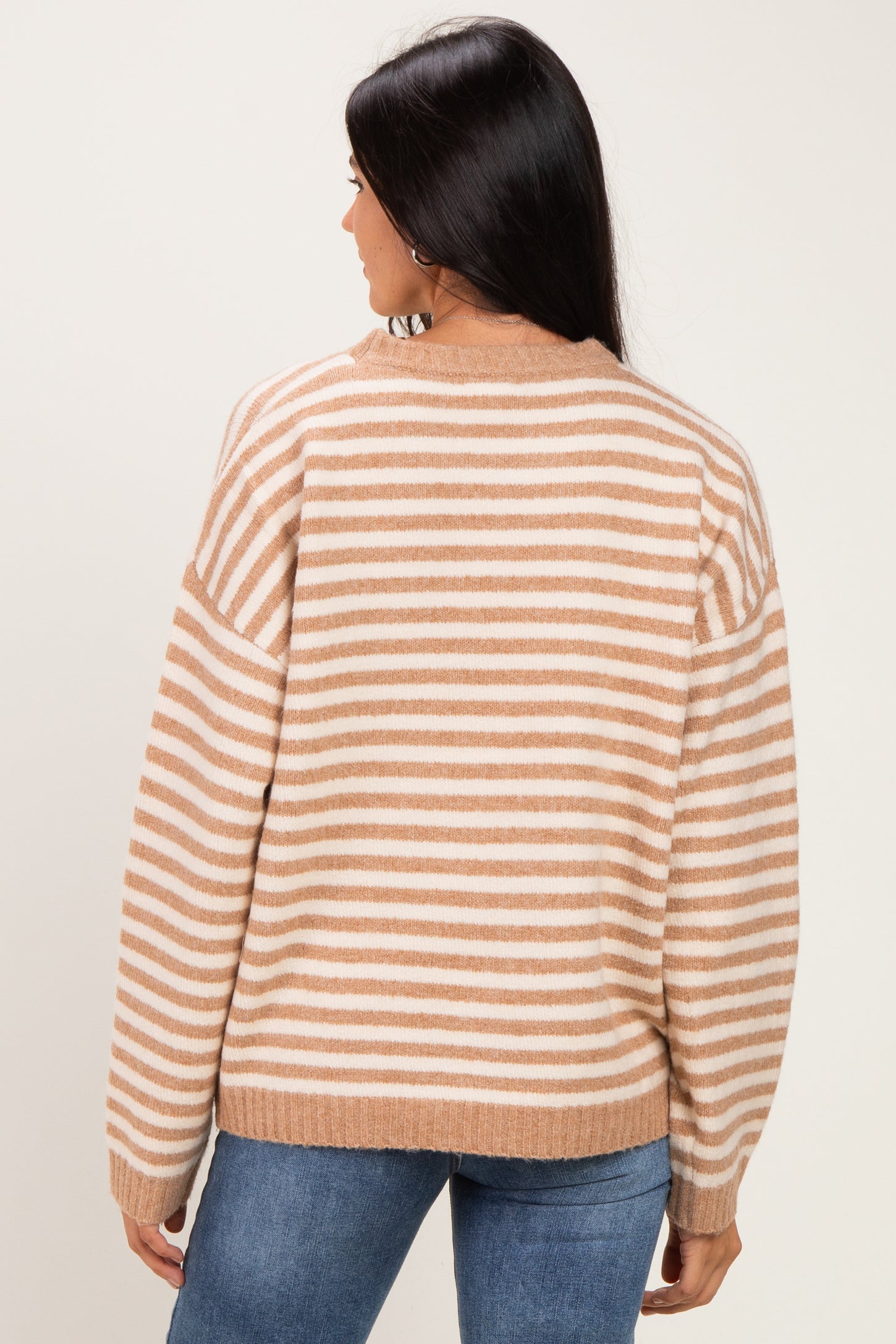 woman wearing a tan and white striped oversized sweater, viewed from the back, paired with blue jeans