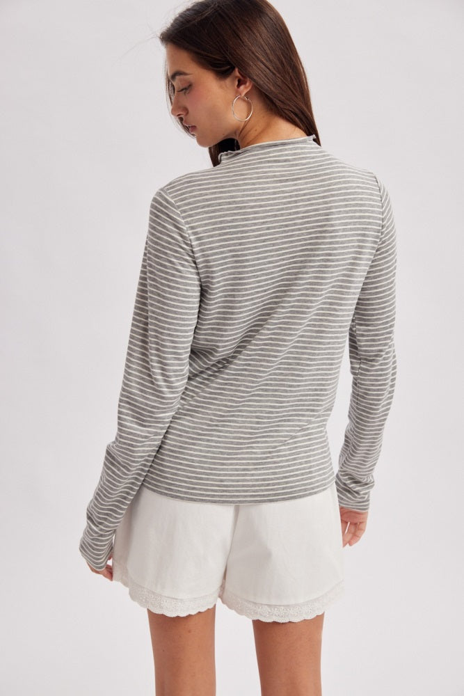 woman wearing a gray and white striped long sleeve top with back view and white shorts