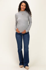 woman wearing a gray and white striped maternity top and holding her baby bump, paired with flared jeans
