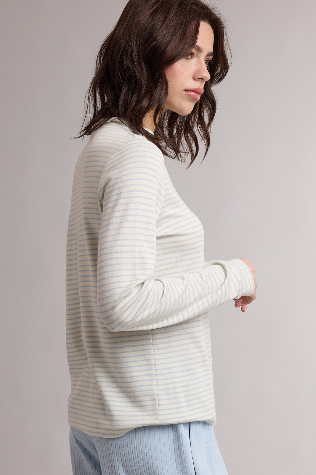 woman wearing a light gray and white striped long sleeve top, shown from the side