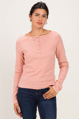 woman wearing a pink and white striped long sleeve henley top with button details and standing against a neutral background