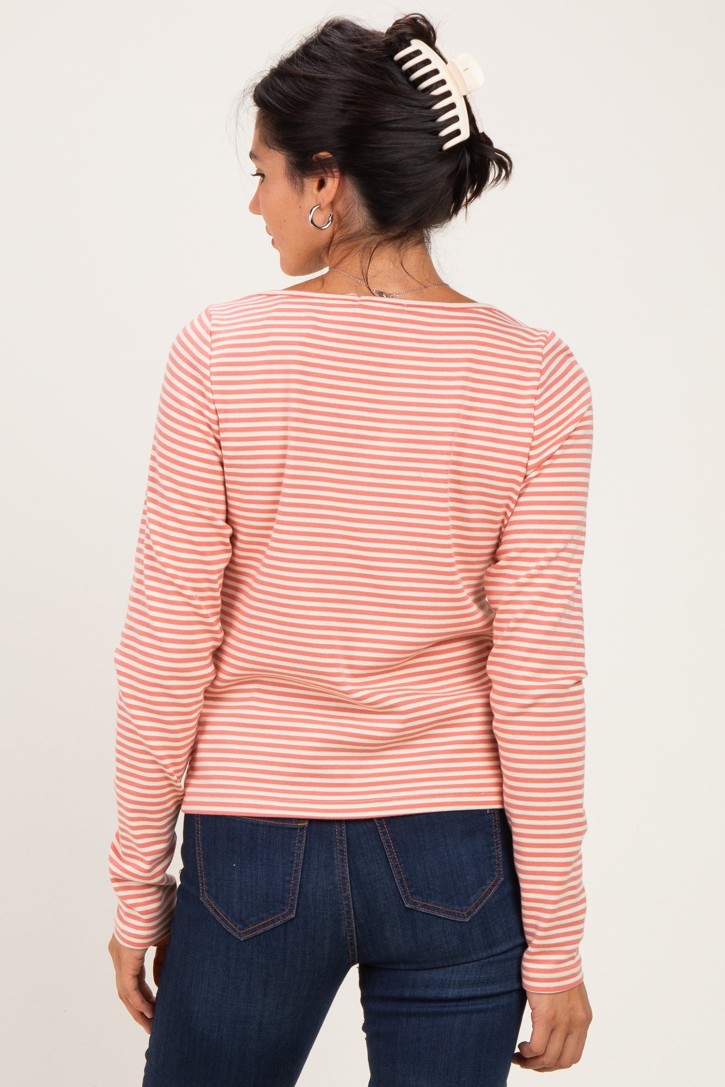 woman wearing a pink and white striped long sleeve top, showing the back view with dark jeans