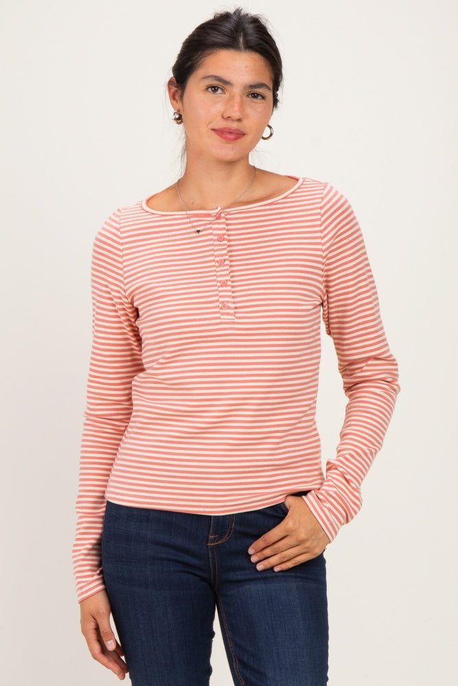 woman wearing a pink and white striped long sleeve henley top with button details and standing against a neutral background