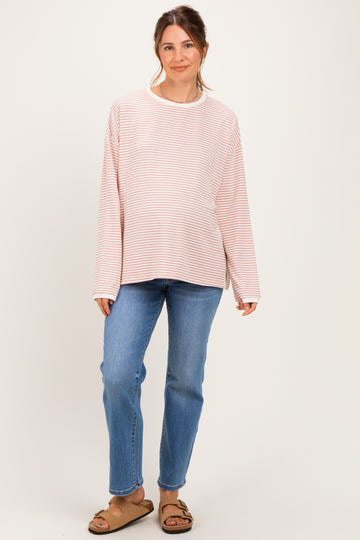 woman wearing a light pink and white striped maternity top with long sleeves and blue jeans, showing her baby bump