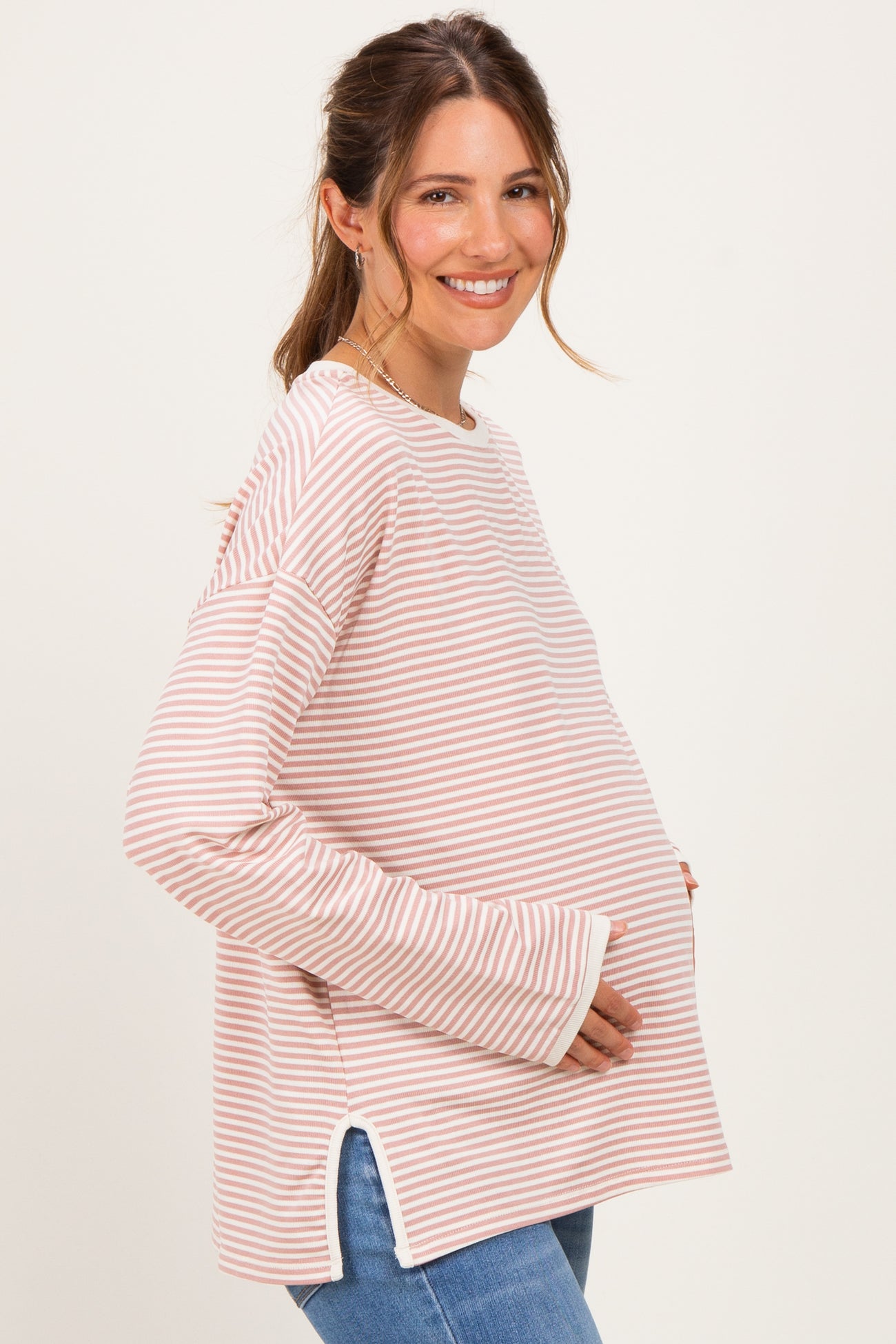 woman wearing a pink and white striped maternity top with side slits and holding her baby bump