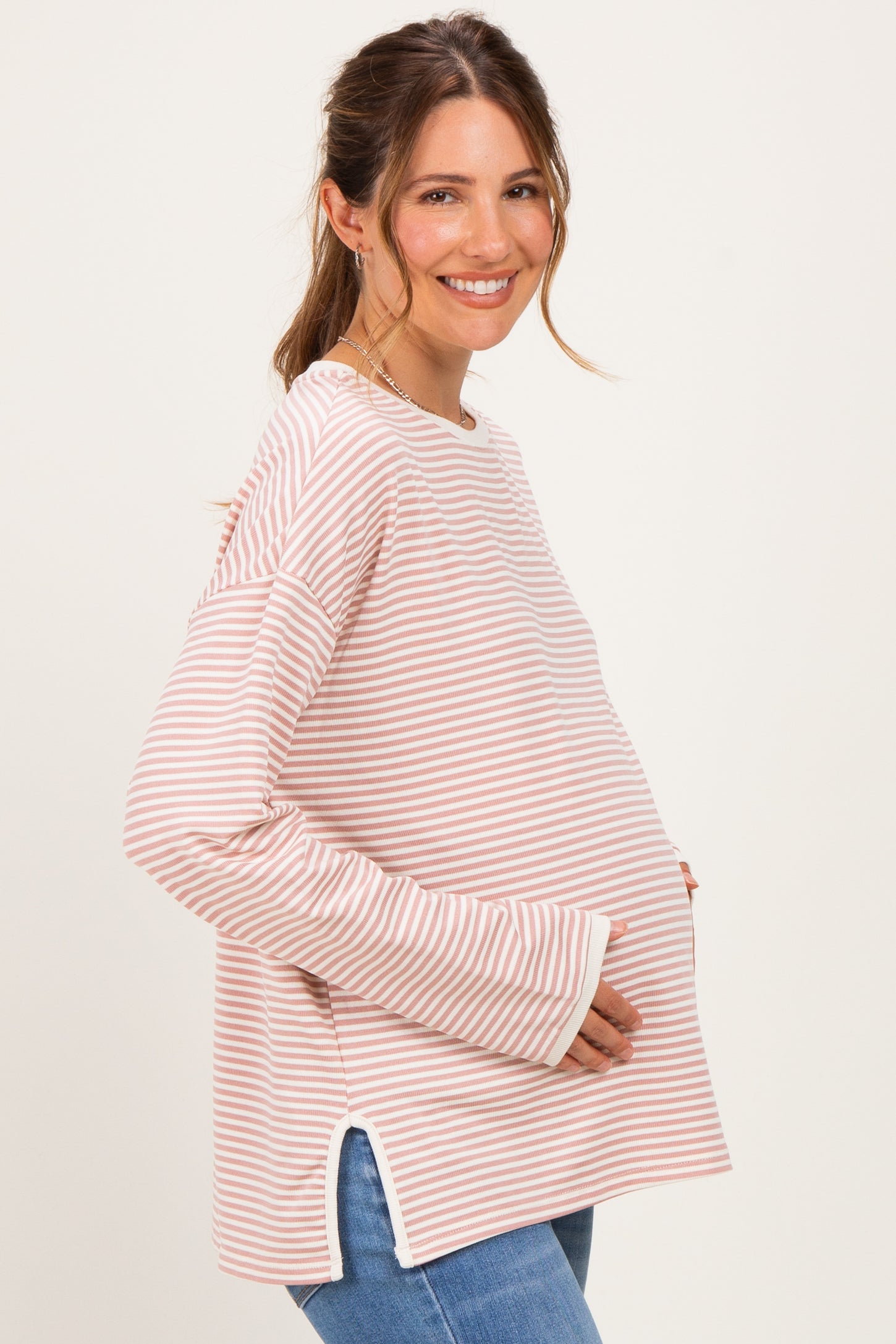woman wearing a pink and white striped maternity top with side slits and holding her baby bump
