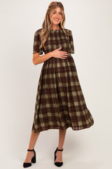 woman wearing a brown and green plaid maternity dress and holding her baby bump
