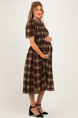 woman wearing a brown and olive green plaid maternity dress and holding her baby bump