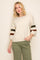 woman wearing a cream oversized sweater with green and brown striped sleeves and olive green pants