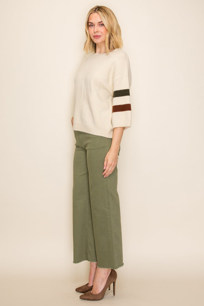 woman wearing a cream oversized sweater with striped sleeves and olive green wide-leg pants, standing in profile with heels